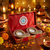 Red velvet box with gold embroidery containing two ornate crystal and metal diya holders for Diwali gift hamper