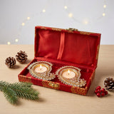 Diwali gift hamper with two ornate gold-toned diya holders embellished with crystals in a red velvet-lined brocade box