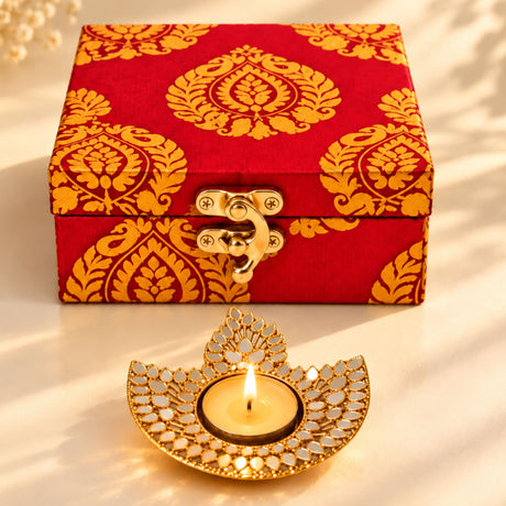 Diwali gift hamper featuring a red and gold brocade box with golden clasp and an ornate mirrored diya candle holder