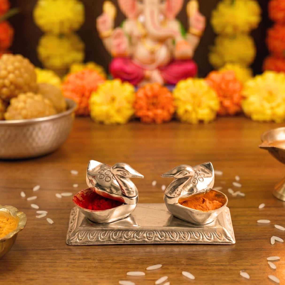 Silver-colored intricately designed bird-shaped containers with open lids holding red and orange powders for Diwali pooja favors