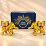 Two vibrant yellow elephant-shaped candle holders with colorful floral embroidery and gold-trimmed bases holding lit green candles for Diwali gifts
