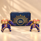 Blue elephant-shaped candle holders with gold accents and colorful striped sashes holding lit tealights for diwali gifts