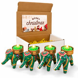Four green elephant-shaped tealight candle holders with gold pink accents holding lit green rose candles for festive gifting