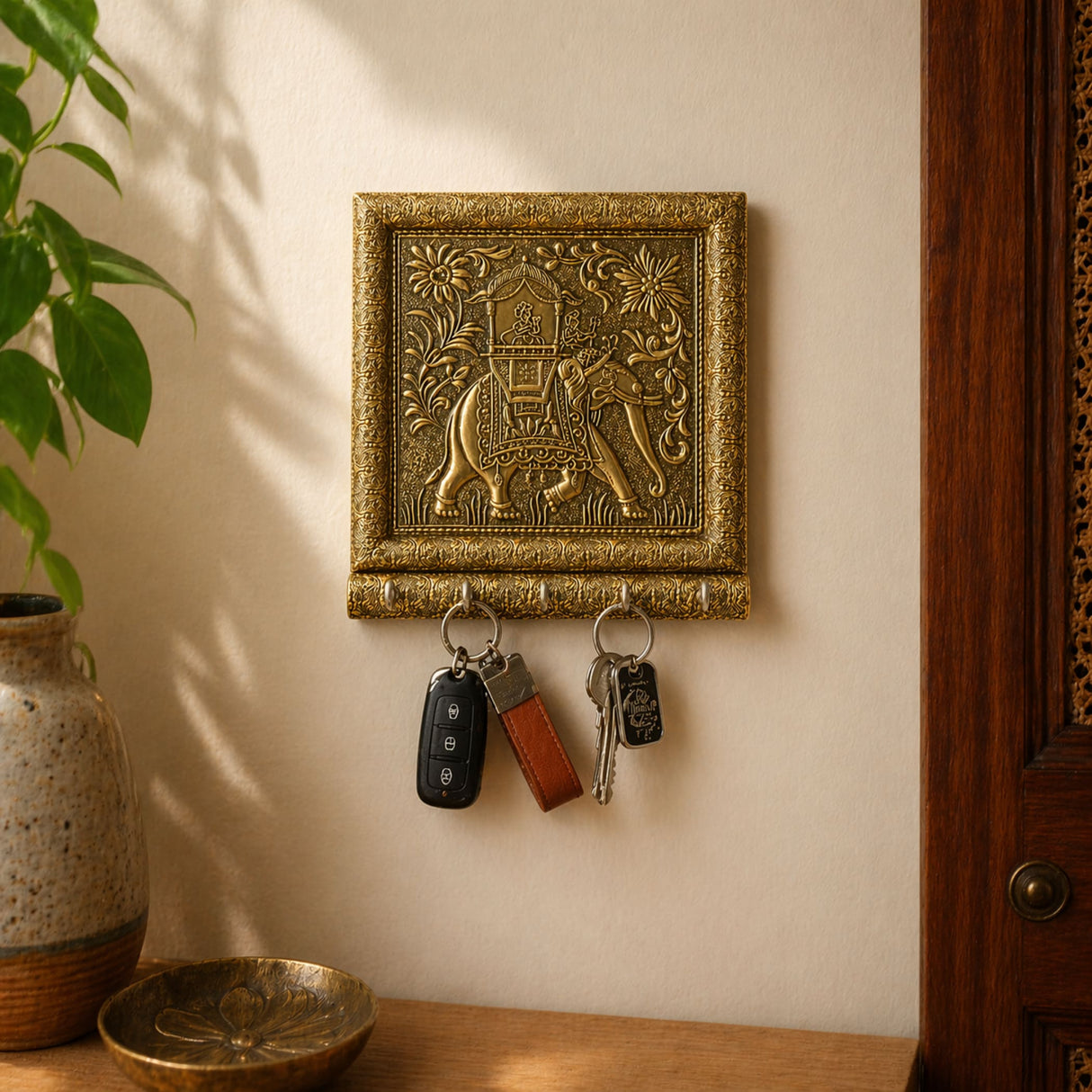 Golden ornate wall-mounted key holder with intricately engraved elephant and floral patterns framed in metallic border