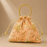 A peach-colored designer potli bag with embroidered gold floral details pearl embellishments and a beaded golden handle
