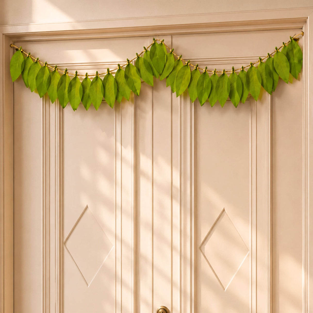 A vibrant green fabric mango leaf door toran hanging with natural veins on gold wire for home pooja decor and celebrations