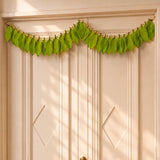 A vibrant green fabric mango leaf door toran hanging with natural veins on gold wire for home pooja decor and celebrations