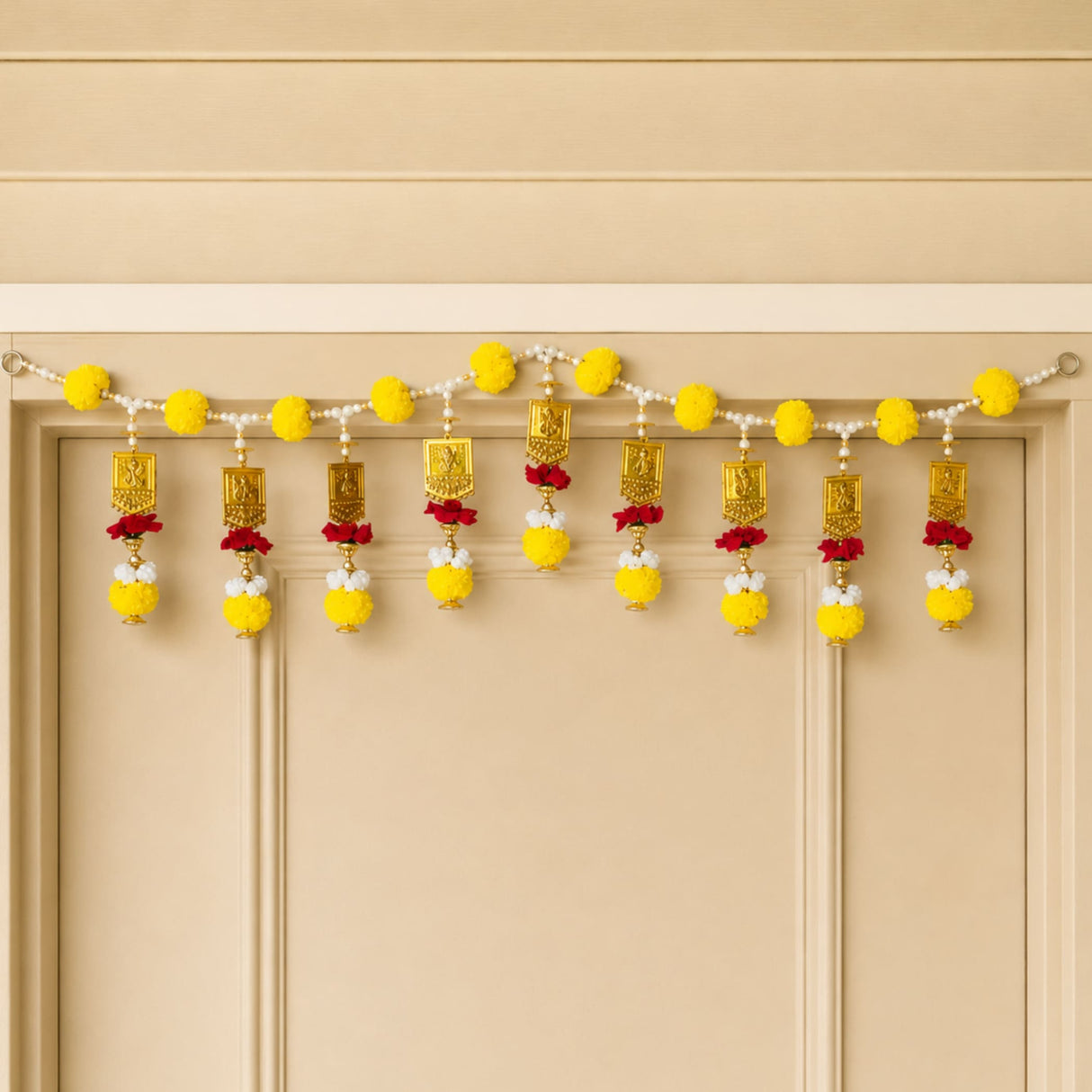 A decorative yellow and gold marigold door toran hanging with beads pom poms and ornamental plaques for pooja decor