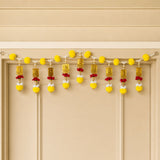 A decorative yellow and gold marigold door toran hanging with beads pom poms and ornamental plaques for pooja decor