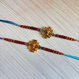 Two designer ganesha rakhi bracelets with golden pendants and reddish-brown wooden beads on turquoise cords for raksha bandhan