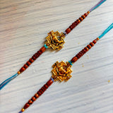 Designer ganesha rakhi featuring golden elephant charms on red beaded bracelets with blue and purple thread ends
