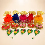 Vibrant orange blue pink red and yellow velvet potli bags with gold-trimmed tops on ornate golden trays for ganesh puja gifts
