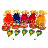 Set of five colorful velvet potli bags with gold lattice patterns and matching trays holding miniature red and pink roses for ganesh chaturthi and diwali gifts