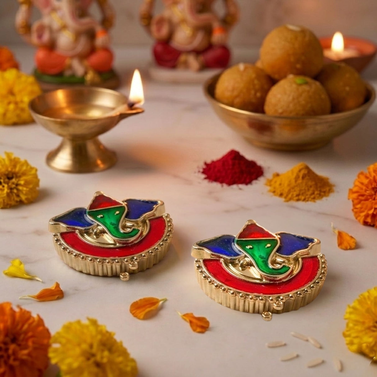 Colorful gold-toned ganesha-themed diya holders with vibrant red bases and green-blue accents for diwali pooja rituals