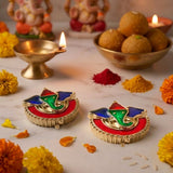 Colorful gold-toned ganesha-themed diya holders with vibrant red bases and green-blue accents for diwali pooja rituals