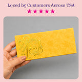 A golden-yellow textured money envelope with embossed ornate design featuring stylized letter r for Indian weddings