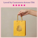 A vibrant yellow paper gift bag with gold foil ganesha design and braided handles for wedding and puja return gifts