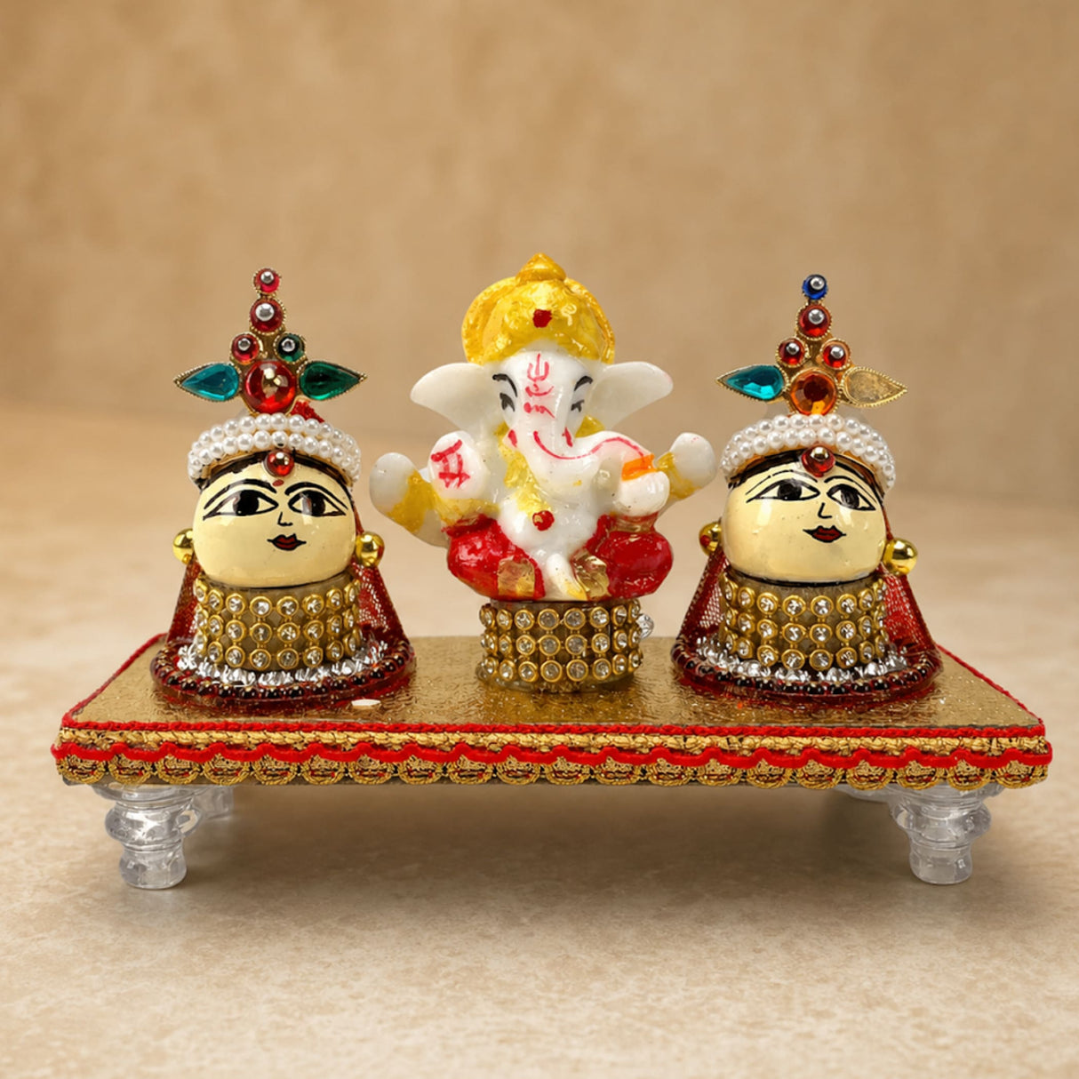 Lord ganesha figurine with golden crown and red attire flanked by riddhi siddhi goddesses adorned in gold and gemstones
