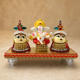 Lord ganesha figurine with golden crown and red attire flanked by riddhi siddhi goddesses adorned in gold and gemstones