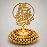 Golden ornamental tealight candle holder with intricate cut-out of figure playing flute and beaded base for festive decor