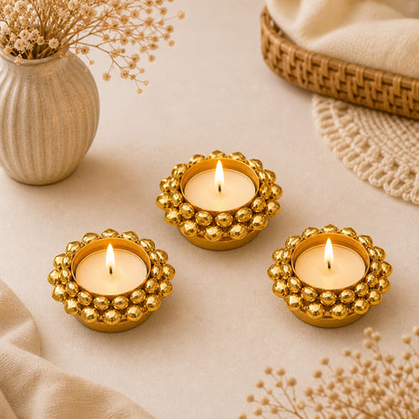 Three golden beaded ghungroo tealight candle holders each with lit candles for diwali and festive decor lighting