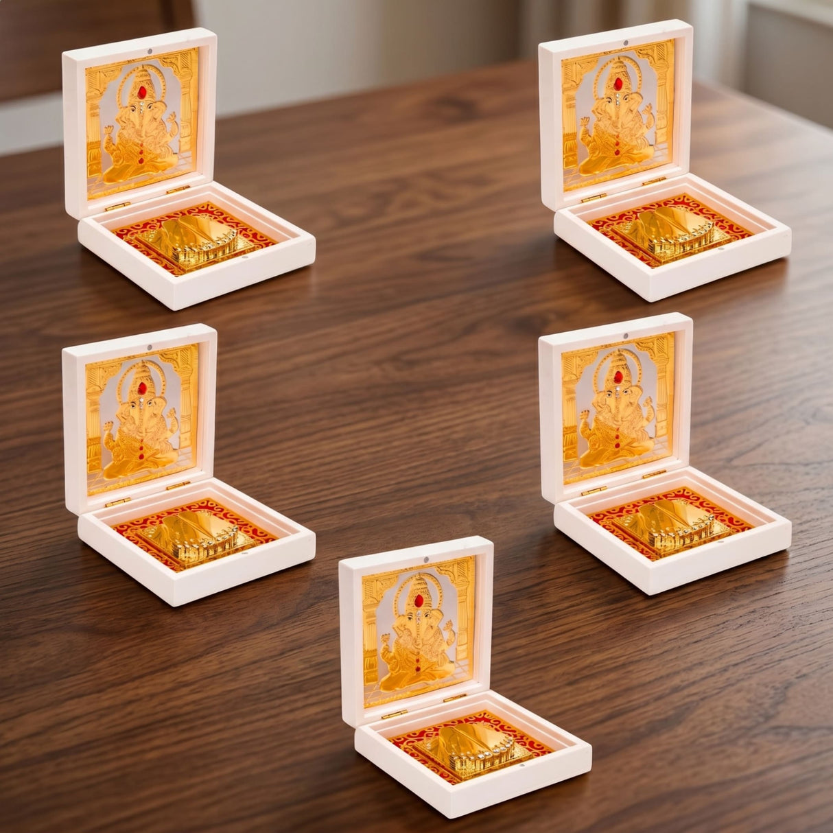 White square boxes each containing a gold plated ganesha figurine with red accents and ornate gold base for pooja decor