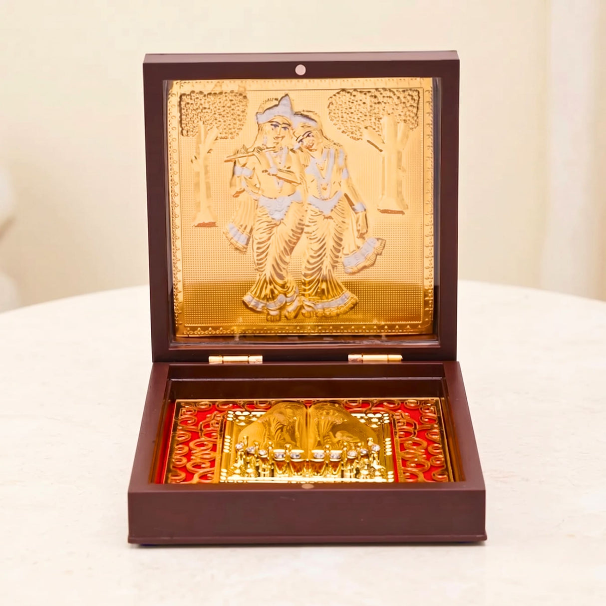 Gold plated ornate box with embossed radha krishna and golden diya on red fabric for diwali pooja décor