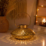 Gold iron tealight candle stand with intricate floral cutouts and circular handle casting warm light patterns