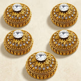 Gold-colored ornate button-like embellishments with intricate filigree and central clear crystal on golden kumkum holder