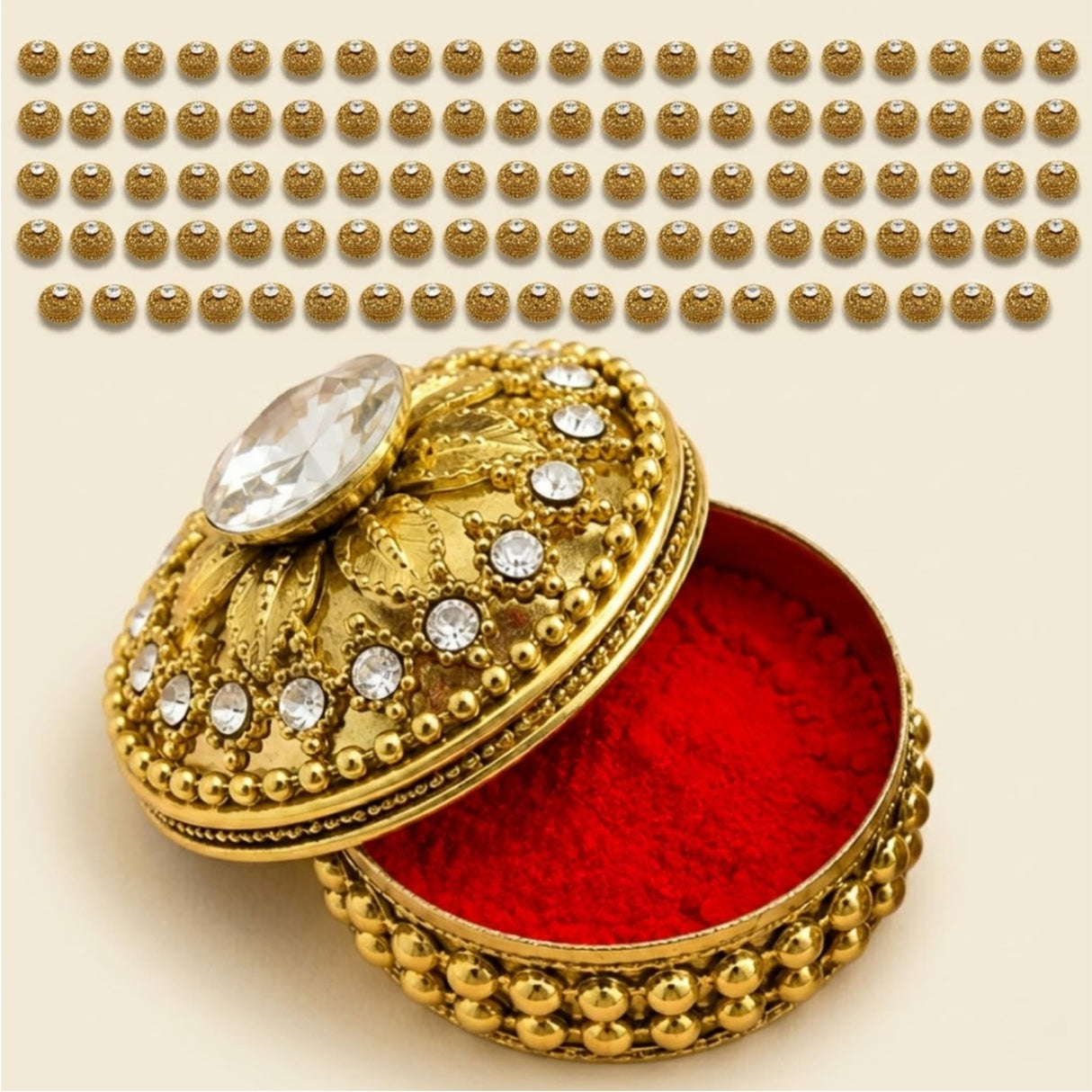 Golden metallic kumkum holder jewelry box with ornate design and clear gemstone lid featuring red velvet interior