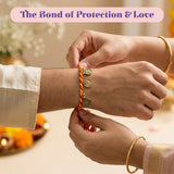 A vibrant red and yellow twisted cord rakhi bracelet with three golden coin charms for raksha bandhan protection