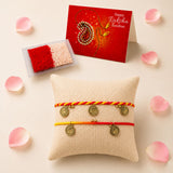 Beige textured pillow displaying two colorful braided rakhi bracelets with gold-toned coin charms for raksha bandhan gift