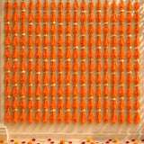 Orange tassels with gold decorative caps hanging in neat vertical rows on gotta patti net backdrop for diwali eid wedding decor