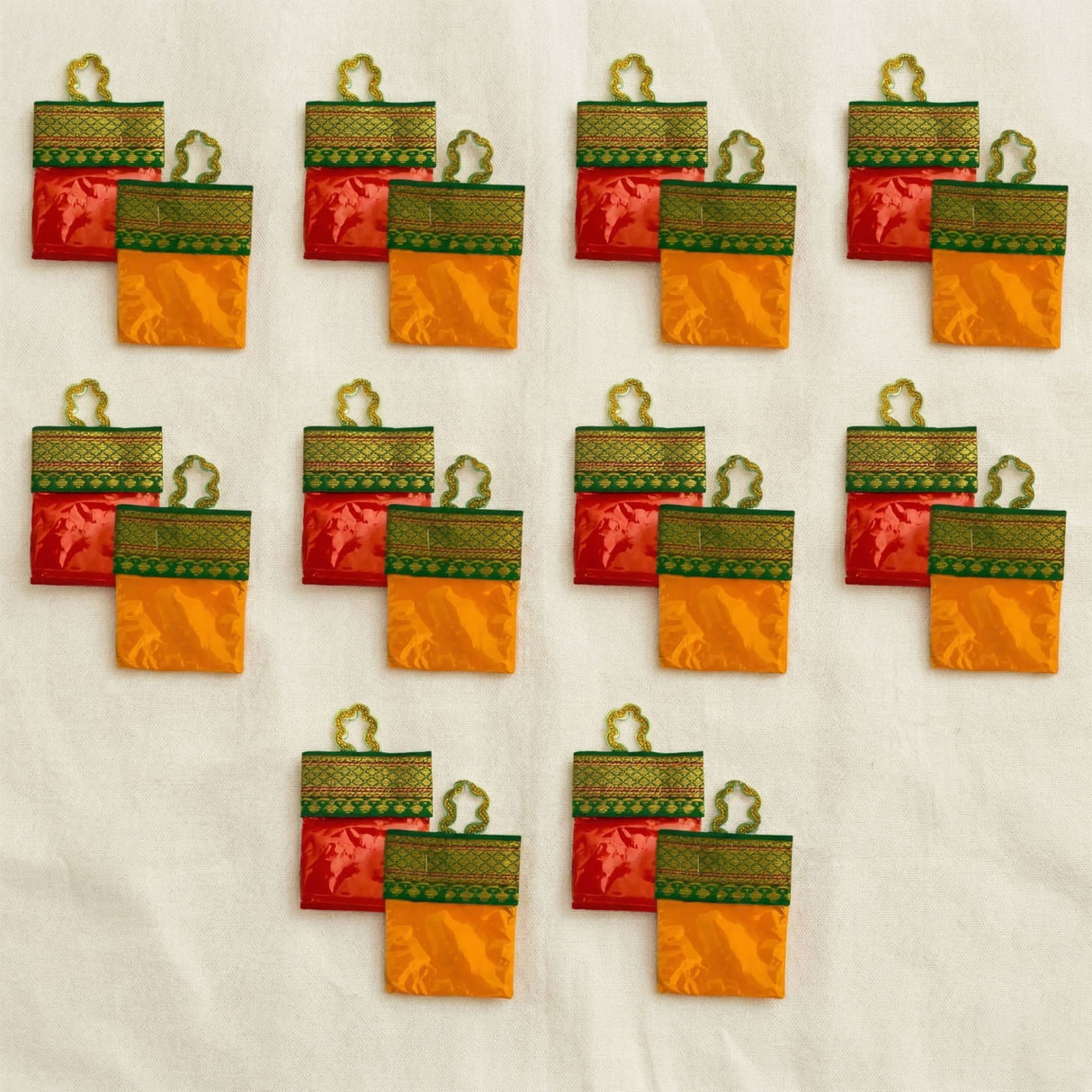 Red and orange satin haldi kumkum packets with green embroidery and gold handles for indian wedding festive essentials