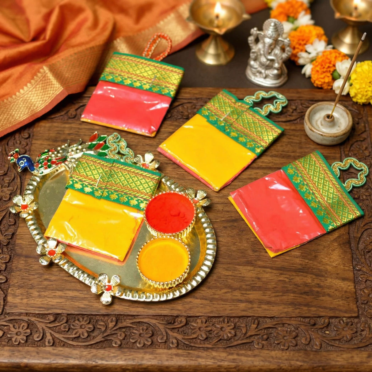 Ornate silver tray with floral designs holding colorful haldi kumkum powders in decorative bowls and patterned pouches for festive use