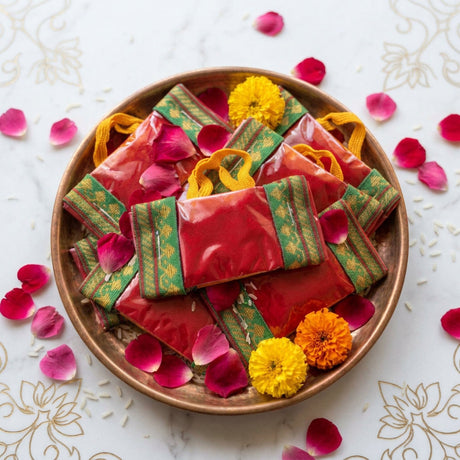 Handbag style mini haldi kumkum packets in red and green patterned paper with yellow handles in a copper bowl for pooja thali gifts