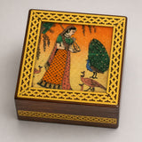 A small square wooden jewelry box with a golden lattice frame and handcarved peacock and woman scene for storage