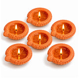 Set of six handmade terracotta clay diyas with intricate floral embossing and lit candles for diwali and pooja decoration
