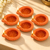Handmade orange terracotta clay diya set with intricate floral embossing and lit candles for pooja and diwali decoration