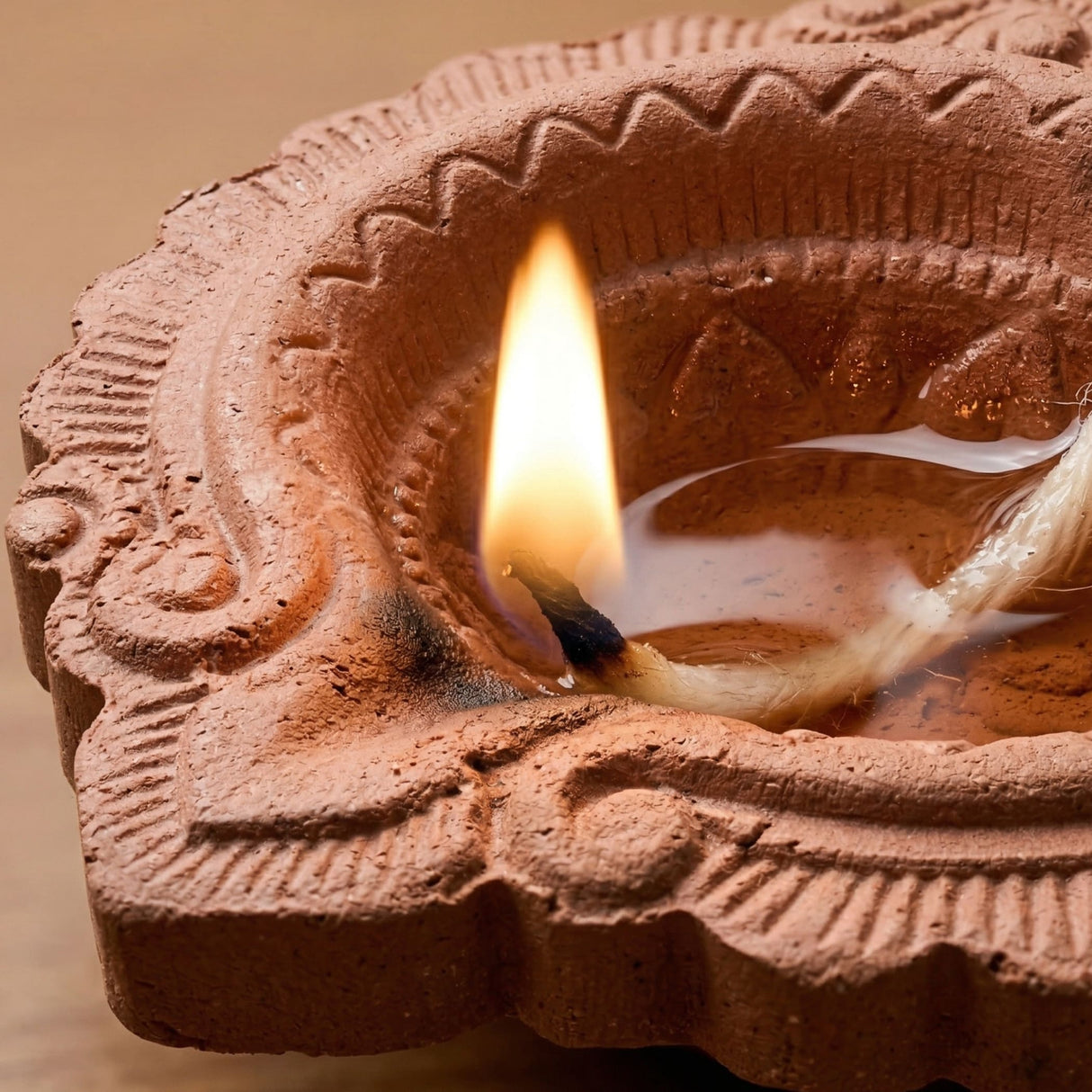 A terracotta clay diya with intricate embossed patterns holding a lit candle for pooja and Diwali decoration