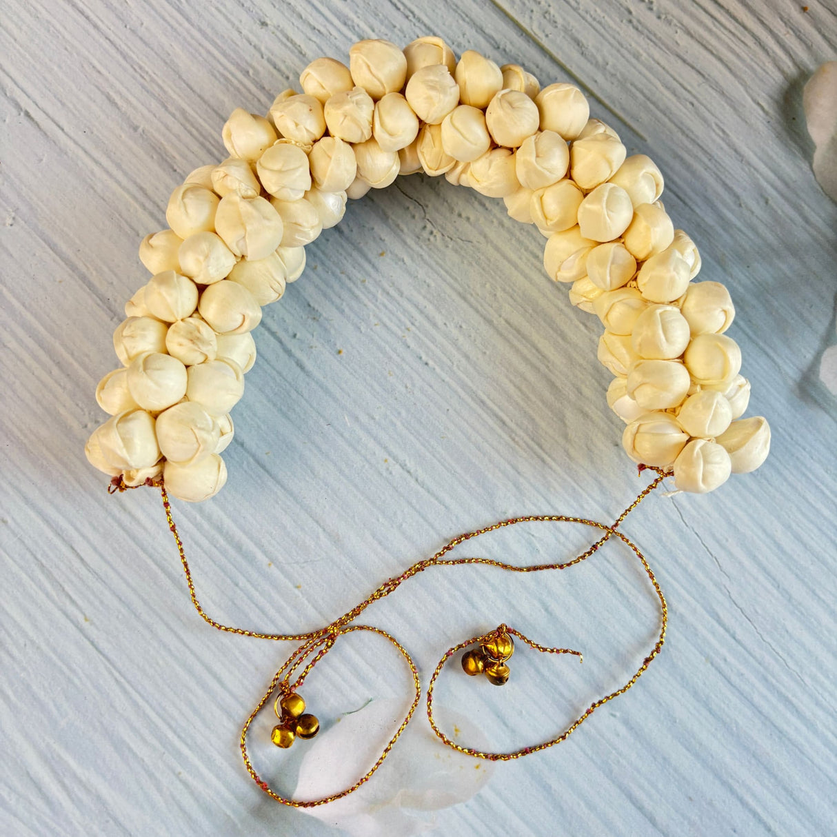 A delicate cream-colored traditional artificial jasmine gajra with fabric petals gold chains and bells for bridal hair accessory