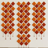 Orange and rust-colored diamond-shaped quilted wall hanging with stitched details and tassels for hindu wedding decor