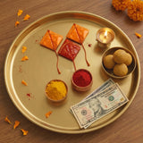 Gold-colored metal tray with haldi kumkum kite style mini packets bowls of colored powders lit oil lamp sweets and us dollar bills for hindu wedding festive essentials