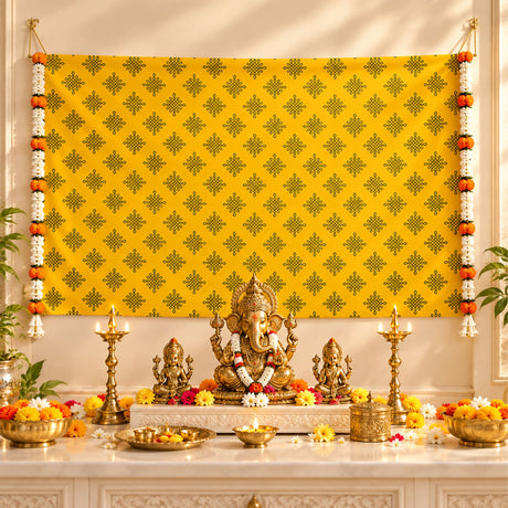 Golden ganesha idol with white and orange floral garland seated on pedestal amid ceremonial items in kolam rangoli backdrop set for pooja and festive decor