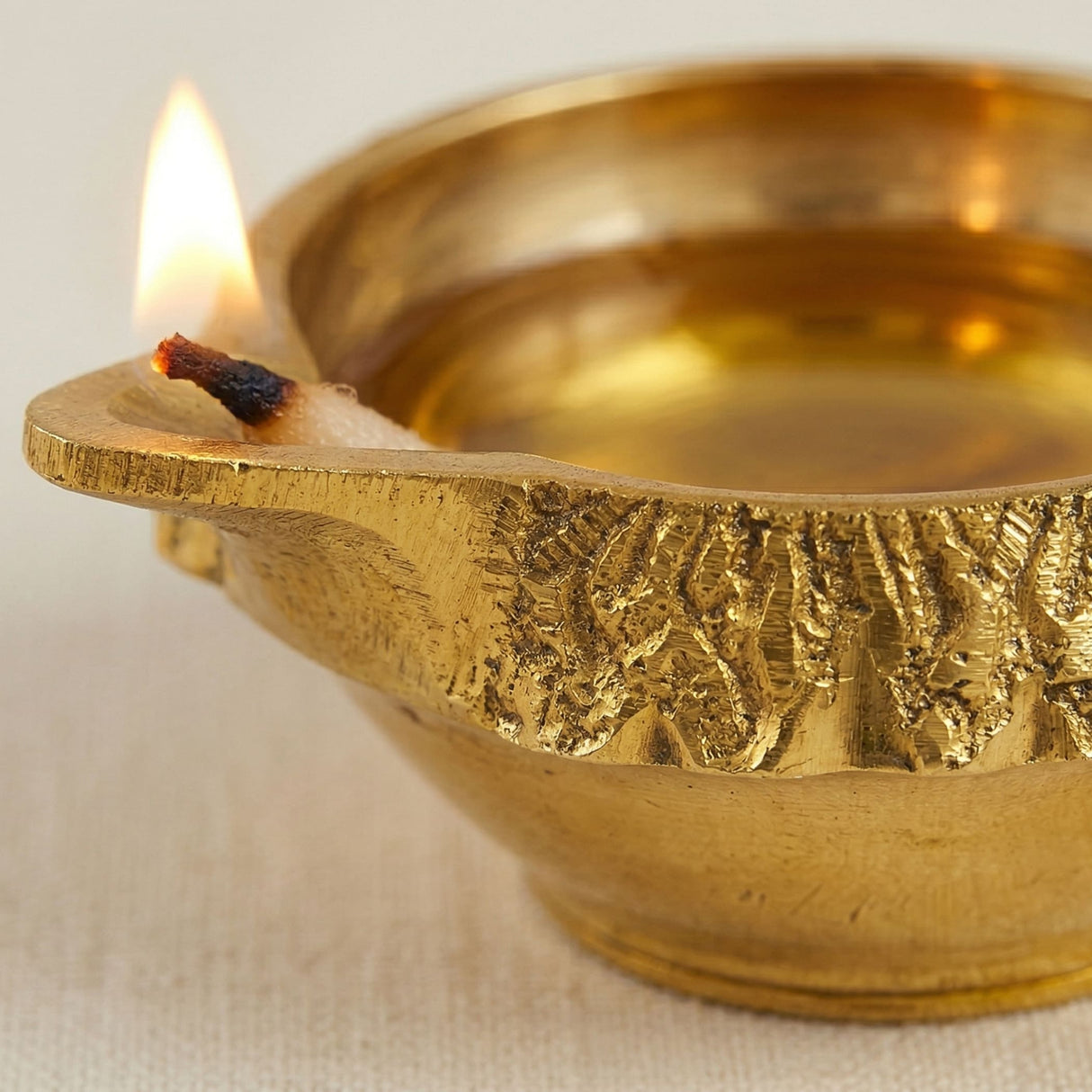 Golden brass kuber diya oil lamp with intricate leaf pattern and lit wick for diwali puja traditional home decor