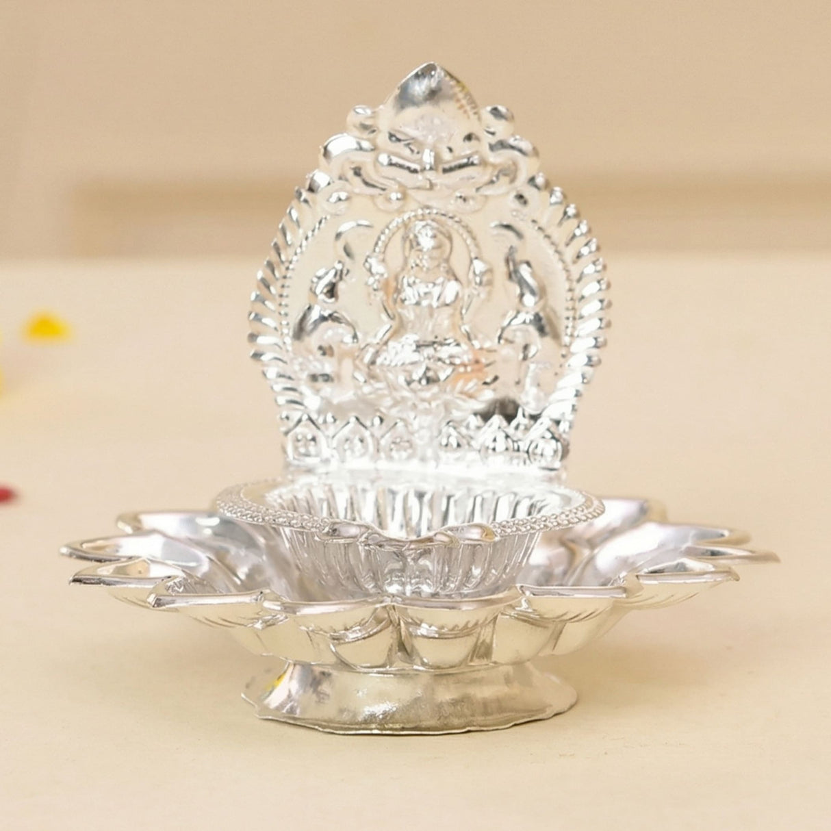 Silver-plated lakshmi diya with intricate embossed seated deity and lotus petal base for puja and diwali decor