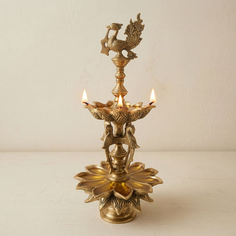 Large parrot brass oil diya with golden brass peacock and lotus designs and three lit candles for puja and decor