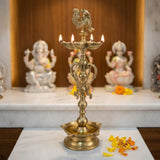 Large golden brass oil lamp with intricate carvings and rooster finial for diwali puja and home decor