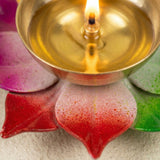 A golden brass lotus diya oil lamp with a lit wick on a colorful ceramic base for home pooja and Diwali decor