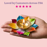 A golden brass lotus diya with a lit candle surrounded by colorful painted leaf petals for Diwali pooja decor